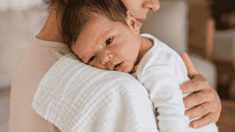A parent gently patting a newborn baby's back to burp them after a feeding