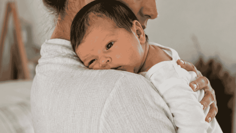 A mother holding her newborn baby upright against her chest after breastfeeding to reduce spit-up