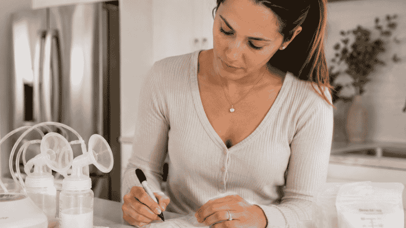A mother labeling a breast milk storage bag with a date after pumping at home
