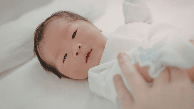 A parent in a dimly lit nursery gently rocking a swaddled newborn in a glider chair, illustrating the reality of nighttime soothing and newborn sleep rhythms.