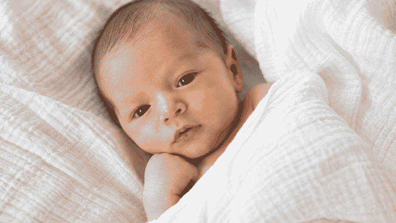 A calm newborn baby lying on a soft blanket after feeding, looking comfortable and content