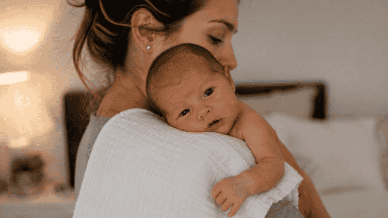A parent holding a newborn baby over their shoulder with a burp cloth after feeding