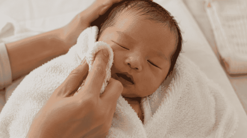 A parent testing newborn bath water temperature with their elbow before bathing the baby