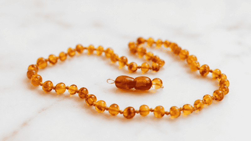 An amber teething necklace displayed on a surface with a warning — these are not recommended by the FDA due to strangulation and choking risks