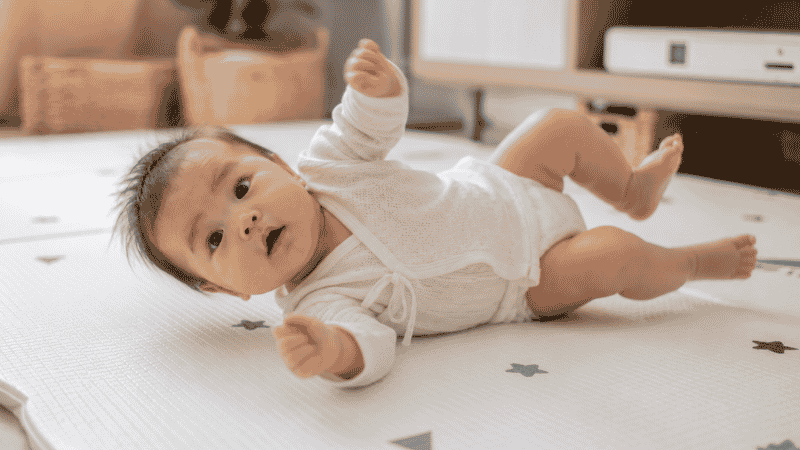 A 4 to 5 month old baby mid-roll from tummy to back on a soft floor mat during playtime