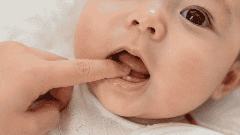 A parent using a clean finger to gently massage a teething baby's swollen gums for pain relief