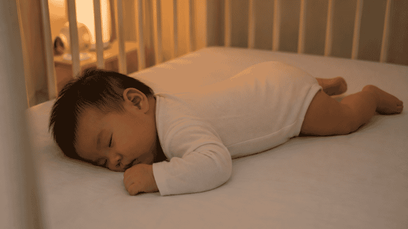 A baby sleeping safely on a firm crib mattress after rolling onto their tummy independently during sleep