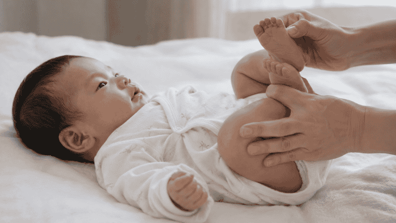 A parent doing bicycle leg exercises with a newborn baby lying on their back to relieve gas