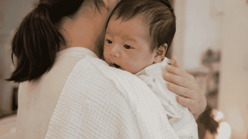 A parent burping a newborn baby over their shoulder with a gentle pat on the back to stop hiccups