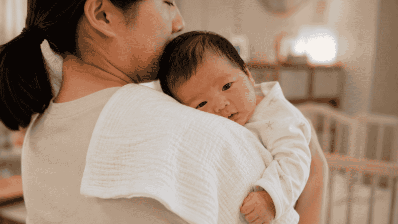 A parent pausing a bottle feeding to burp their newborn baby mid-feed to prevent gas buildup
