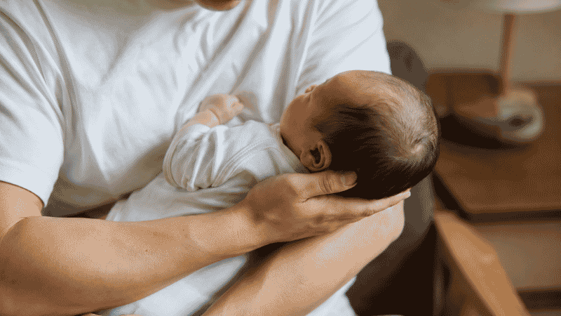 A first-time parent holding their newborn baby carefully at home, looking calm and loving