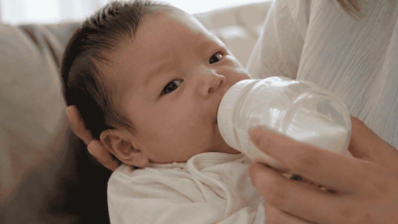 A newborn baby feeding from a bottle, showing the feeding position that can lead to swallowing air and hiccups
