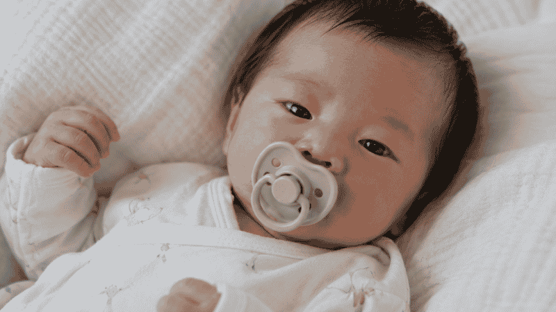 A newborn baby sucking on a pacifier to help calm hiccups and relax the diaphragm