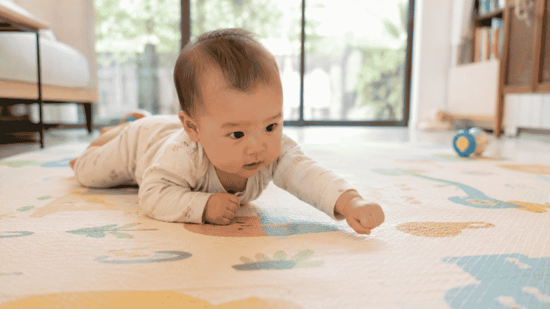 A baby doing a belly crawl or commando crawl across the floor using their arms to pull forward