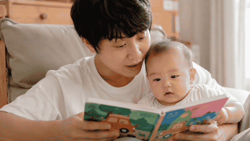 A parent reading a colorful board book aloud to their baby to support early language and speech development