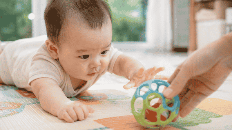 A parent placing a colorful toy just out of reach to motivate a baby to crawl toward it during floor play