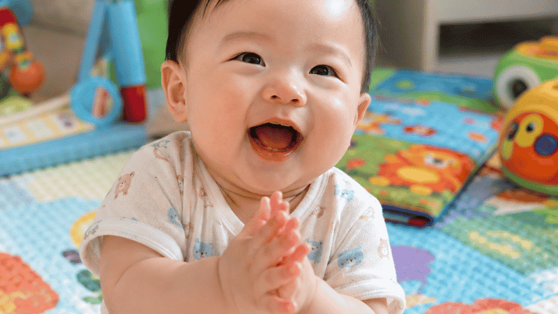 A baby around 9 months old clapping their hands together with an excited expression during play
