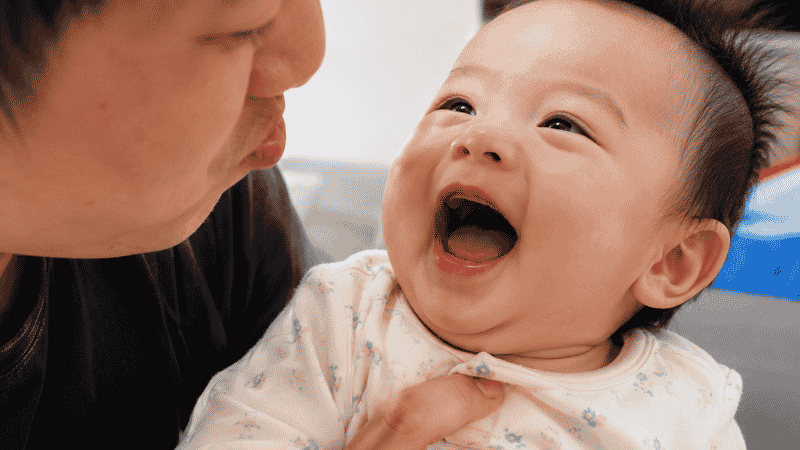 A baby around 4 months old laughing with mouth open during playful interaction with a parent