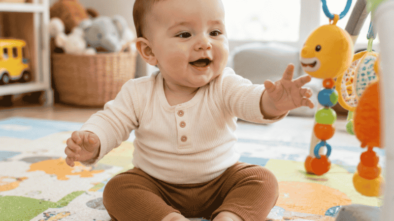 A baby around 7 months old sitting independently with both hands free to play with a toy
