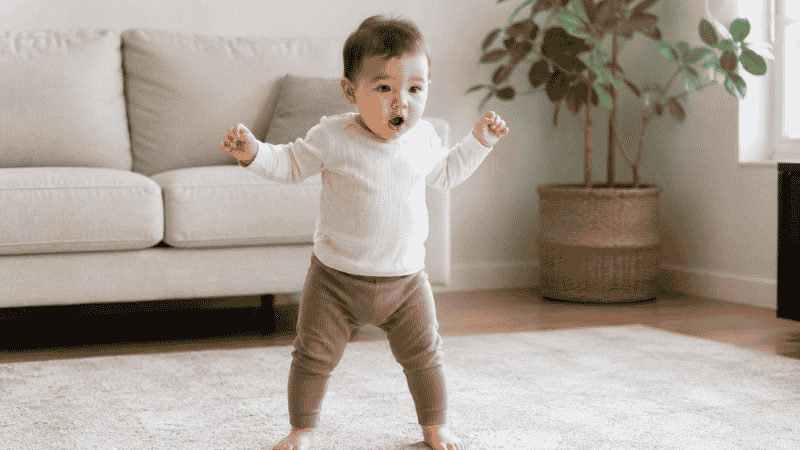 A baby standing independently without holding onto anything for the first time, looking surprised and proud