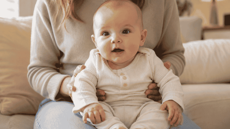 A parent supporting a young baby in a sitting position on their lap to practice sitting with support