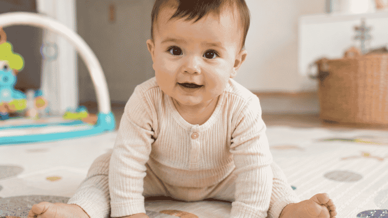 A baby in the tripod sitting position with both hands on the floor for balance support at around 5 to 6 months old