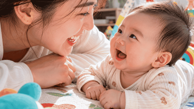 A parent and baby engaged in face-to-face interaction with eye contact and warm smiles, supporting social development